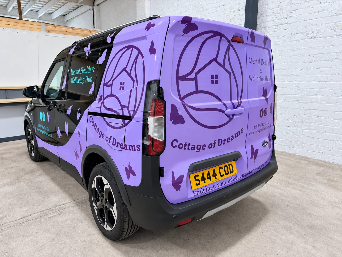 Rear-quarter view of the Cottage of Dreams black van with purple partial wrap, house logos, butterfly graphics and vinyl lettering.