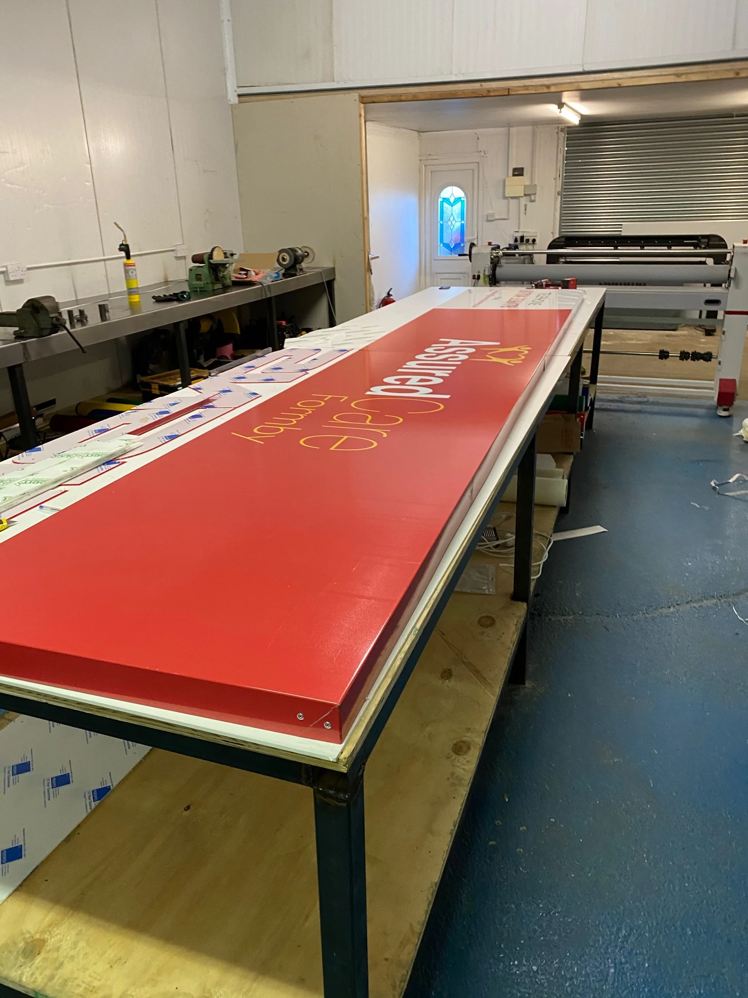 Red Assured Care Formby sign tray with vinyl graphics on the workshop bench