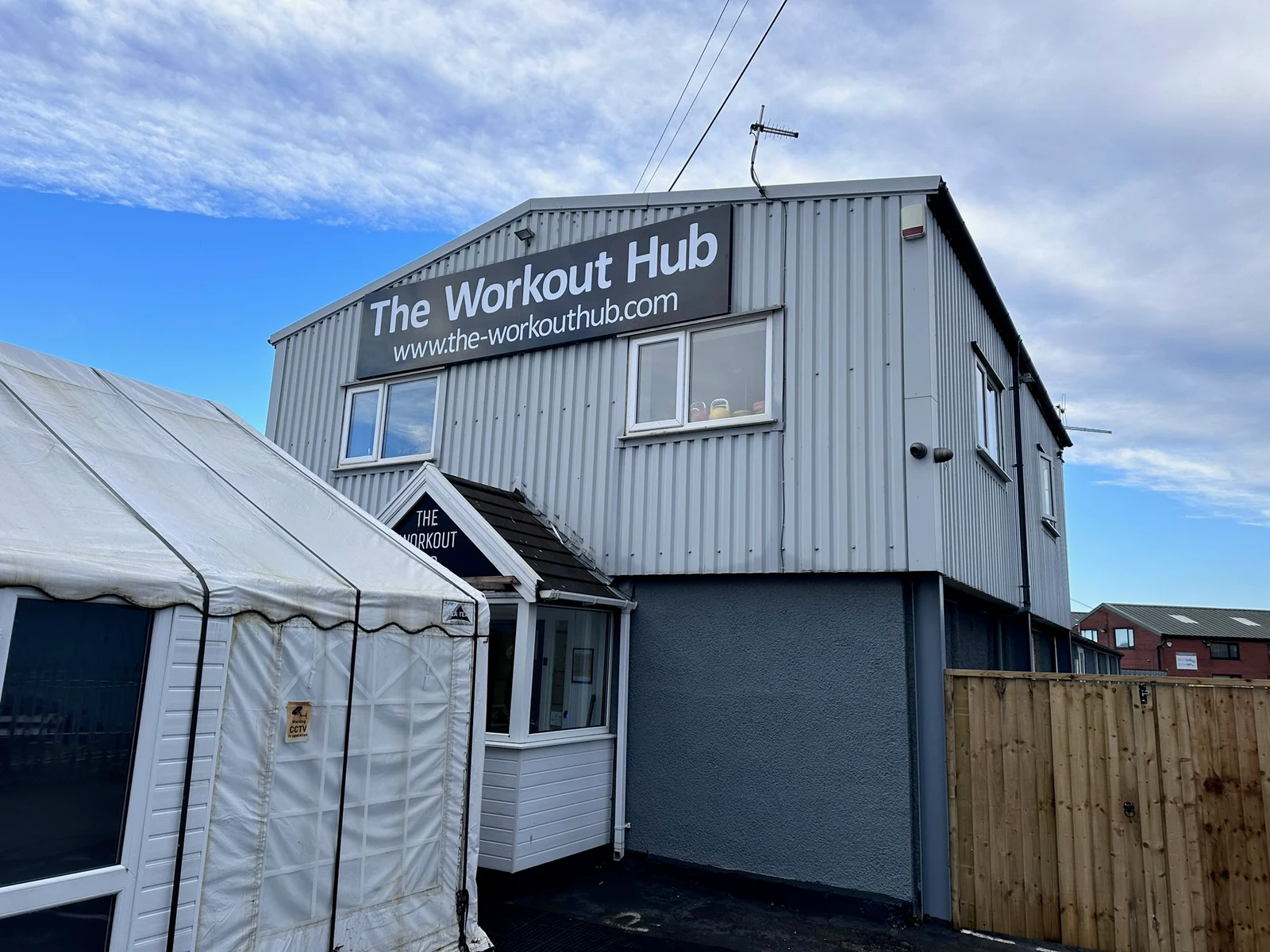 Dark sign tray with white Workout Hub name and website on a grey building