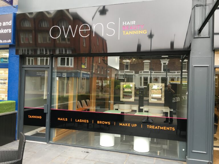 Salon shopfront with branded vinyl lettering and a black promotional strip across the windows